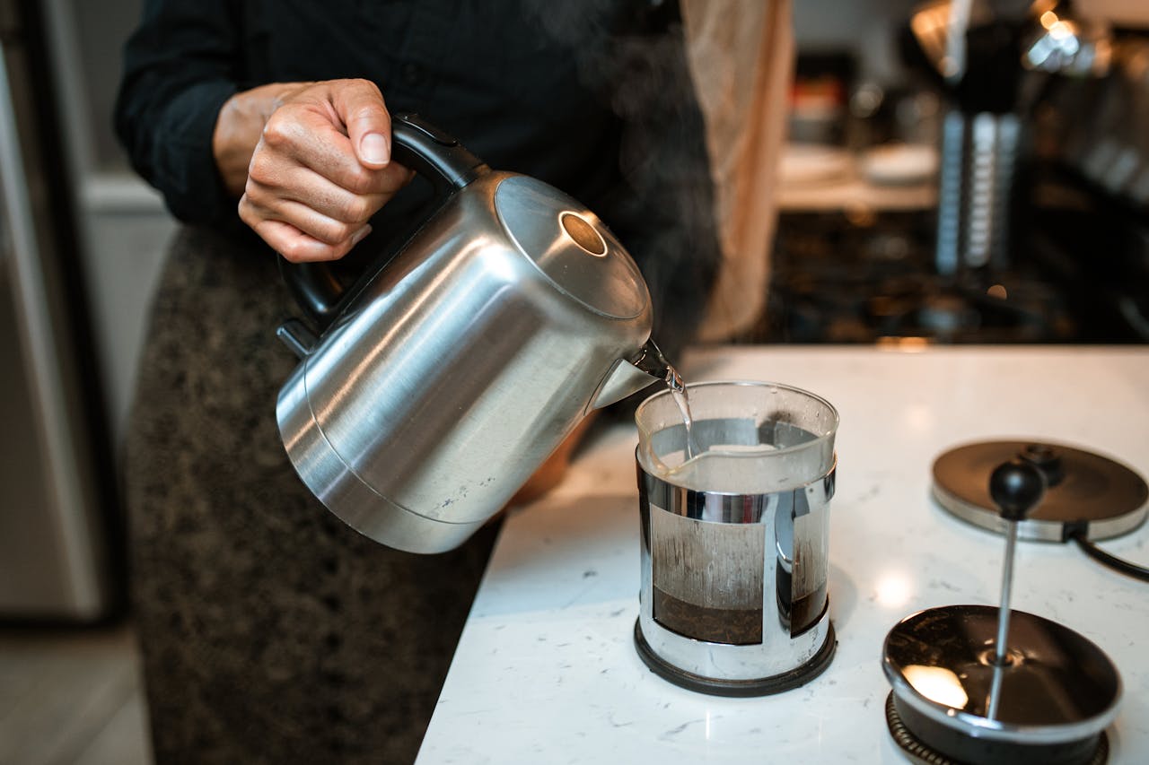 Close-up of pouring hot water into a French press in a modern kitchen setting.